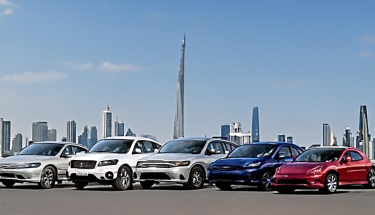 A group of electric vehicles parked with the city skyline in the background, featuring five different cars in white, silver, blue, and red.