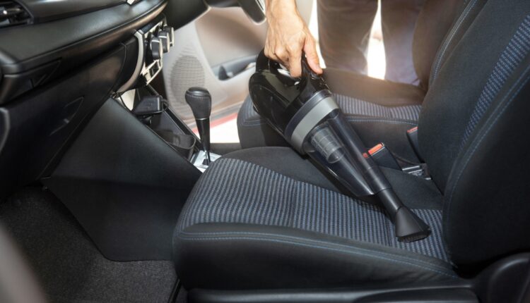 Handheld vacuum cleaning the front car seat during interior detailing