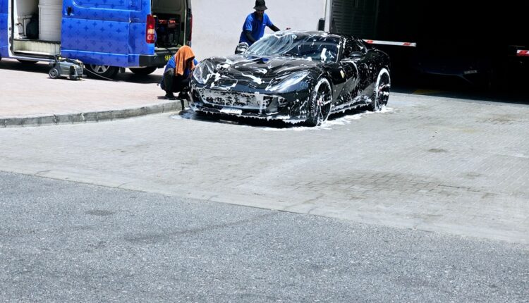 A professional car wash service in Dubai with staff cleaning a shiny black SUV under bright daylight.