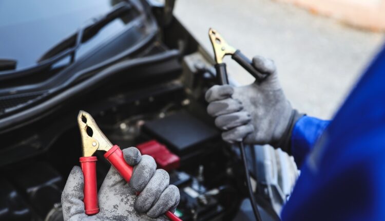Gloved hands holding jumper cables near a car battery for jump start.