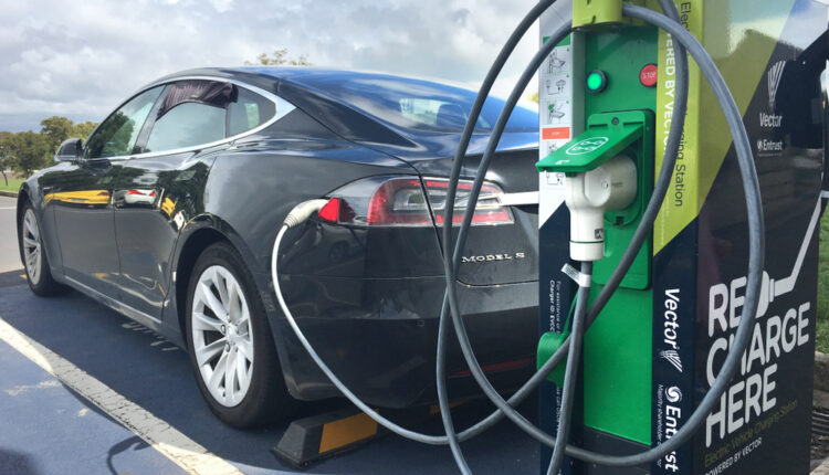 Tesla electric car charging at a public EV charging station during the day.
