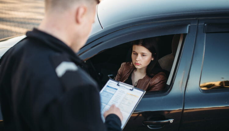 Police officer handing traffic violation ticket to a woman driver seated in a car.