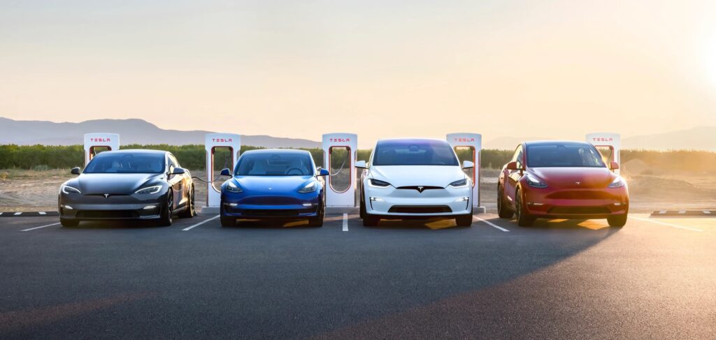 Used Tesla cars charging at Superchargers in UAE – Tesla Model 3, Model Y, Model S, and Model X parked under sunset.