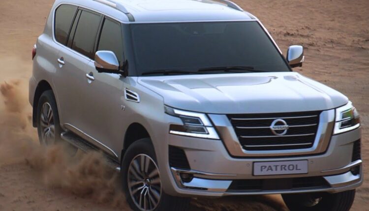 A silver Nissan Patrol SUV driving through desert sand, showcasing its off-road capability.