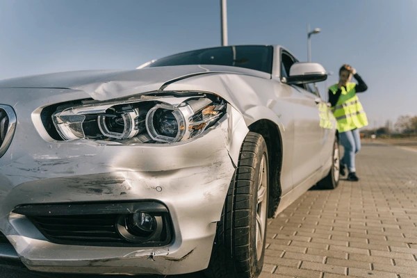 White car with front-end damage parked on the roadside and traffic officer inspecting the scene in Dubai