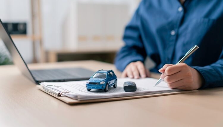 Person filling car registration renewal form with laptop, car model, and key on desk.