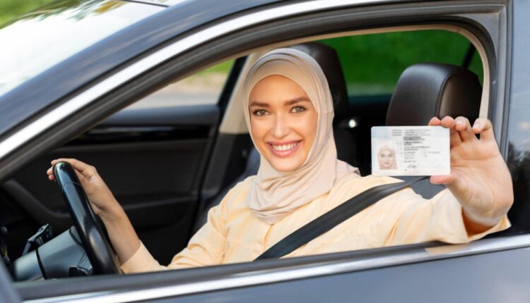Smiling woman in a hijab sitting in a car holding her driving licence card, representing successful Dubai driving licence management.