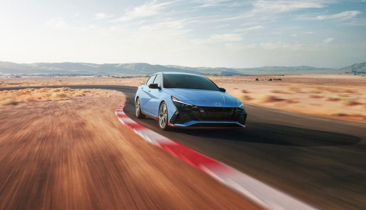 A blue Hyundai sedan driving swiftly on a curved desert track under a bright sky, representing Hyundai Elantra’s resale value and long-term reliability in Dubai conditions.