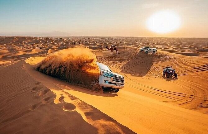 SUV carves a dune at golden hour in a UAE desert, towering sand plume, camels and support vehicles behind, showcasing car photography in the UAE during cooler months.