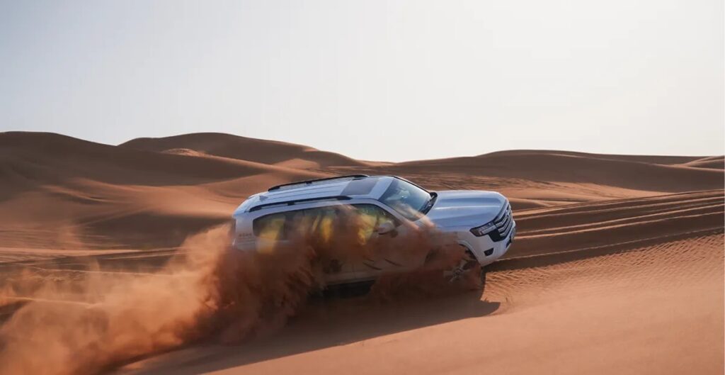 Toyota SUV driving across UAE desert dunes demonstrating KDSS suspension, Crawl Control, and Multi-Terrain Select technologies.