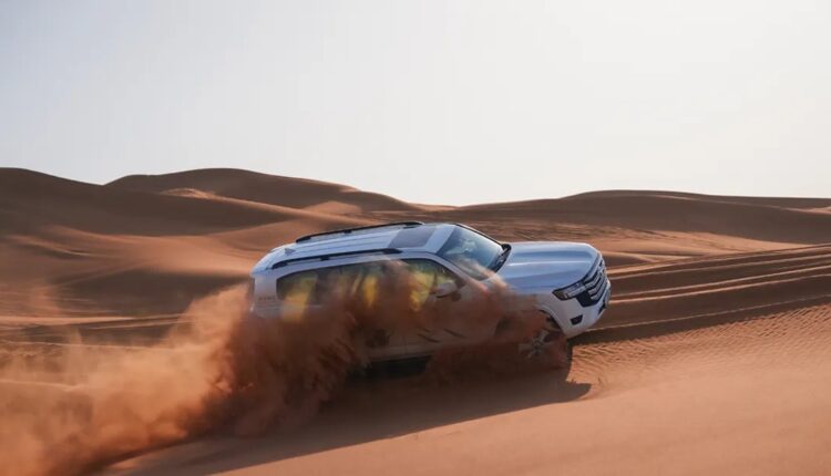 Toyota SUV driving across UAE desert dunes demonstrating KDSS suspension, Crawl Control, and Multi-Terrain Select technologies.