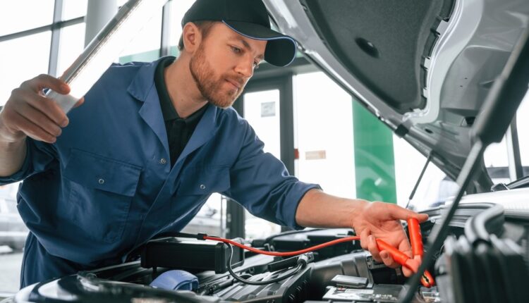 Mechanic inspecting a car battery and using jumper cables inside a service workshop in the UAE