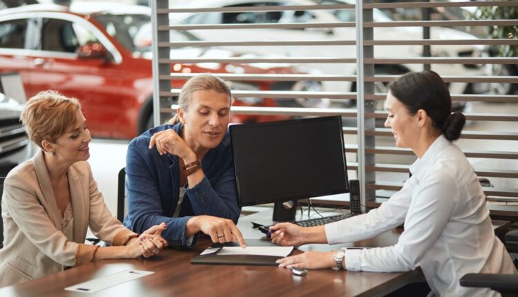 A couple discussing car leasing options with a consultant at a dealership desk.