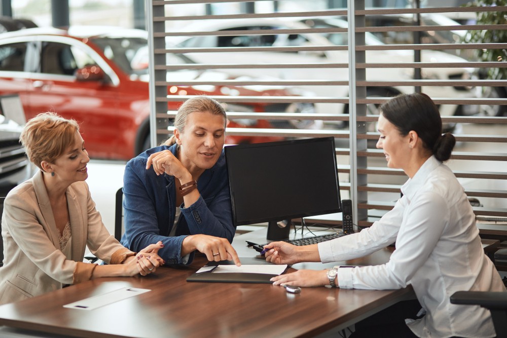 A couple discussing car leasing options with a consultant at a dealership desk.