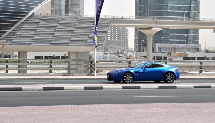 Blue sports car driving in Dubai under bright sunlight, showcasing car paint exposed to UV rays and sandy conditions.