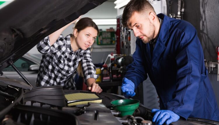 Mechanic explaining car fluid checks to a driver during a routine engine inspection.