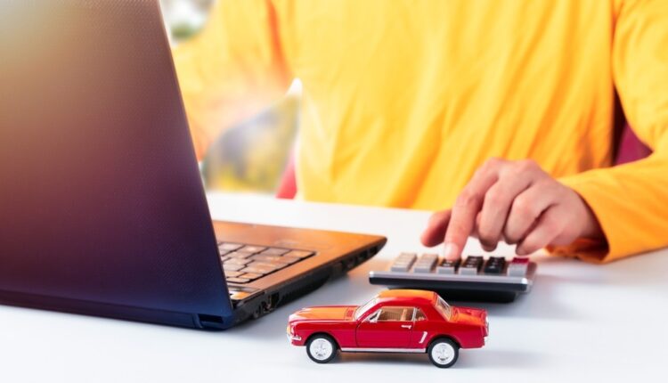 A person using a laptop and calculator to analyze car depreciation with a toy car on the desk.
