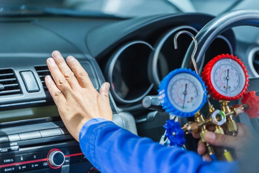 Technician checking car AC cooling with pressure gauges during a Car AC Gas Refill service in the UAE.