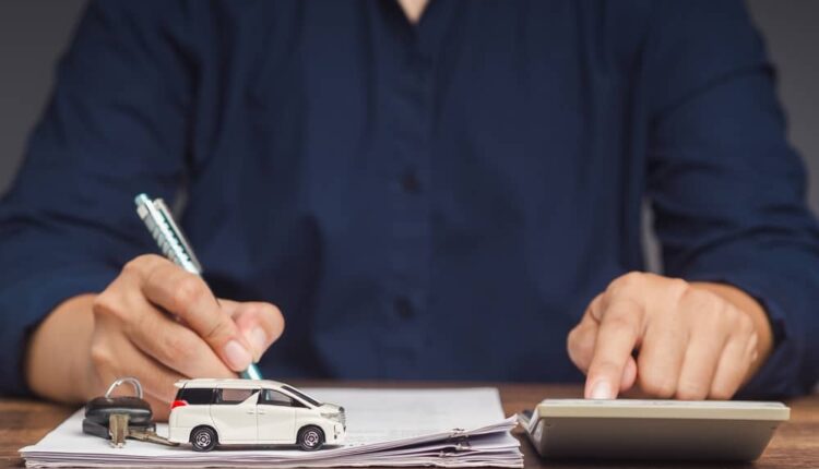 Person calculating finances with a toy car and documents, comparing cash vs loan for used car purchase in the UAE.