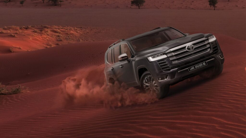 Toyota Land Cruiser 300 driving through red desert dunes in the UAE.