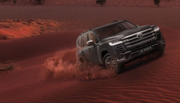 Toyota Land Cruiser 300 driving through red desert dunes in the UAE.