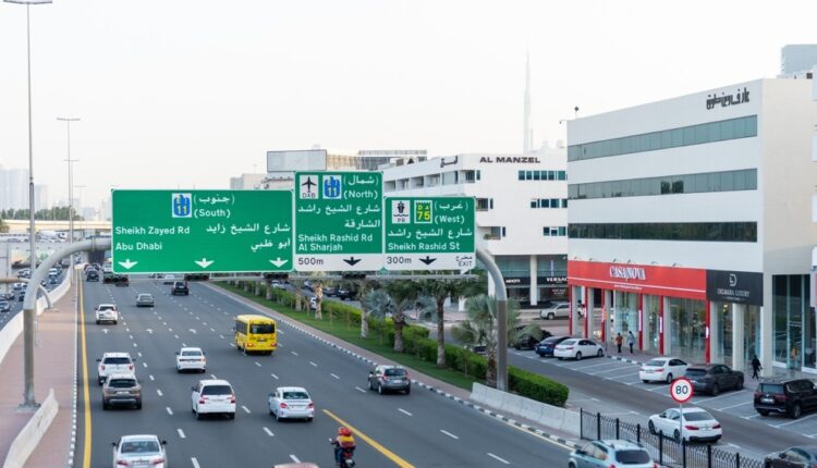 Road sign on Sheikh Zayed Road, showing directions to Abu Dhabi and Al Sharjah with clear traffic signs visible in the background.