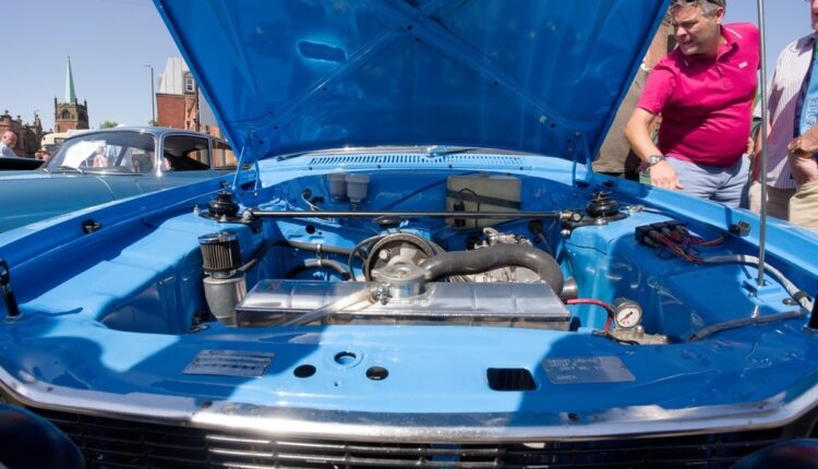 "Checking the engine coolant reservoir under the hood of a classic car without opening the radiator cap.