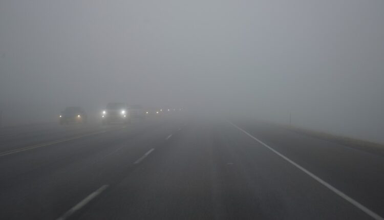 Winter driving in UAE: Car driving through thick fog on a deserted road, highlighting reduced visibility and the challenge of foggy conditions on UAE roads.