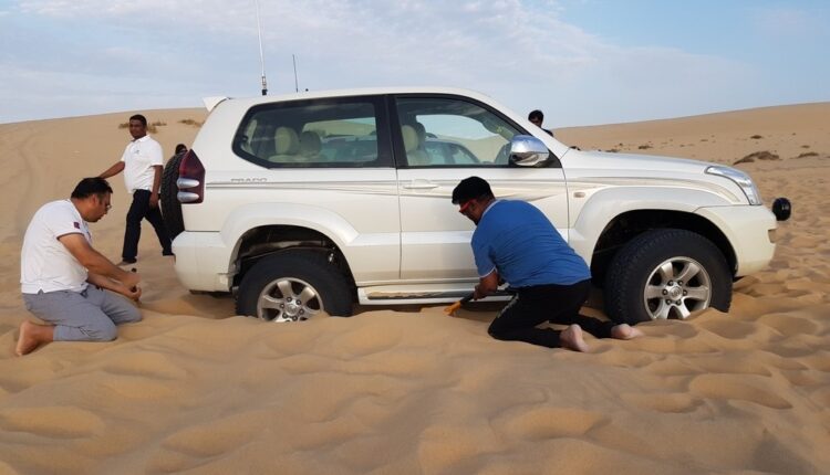 Off-roading recovery: two people digging around a stuck 4×4 in the desert.