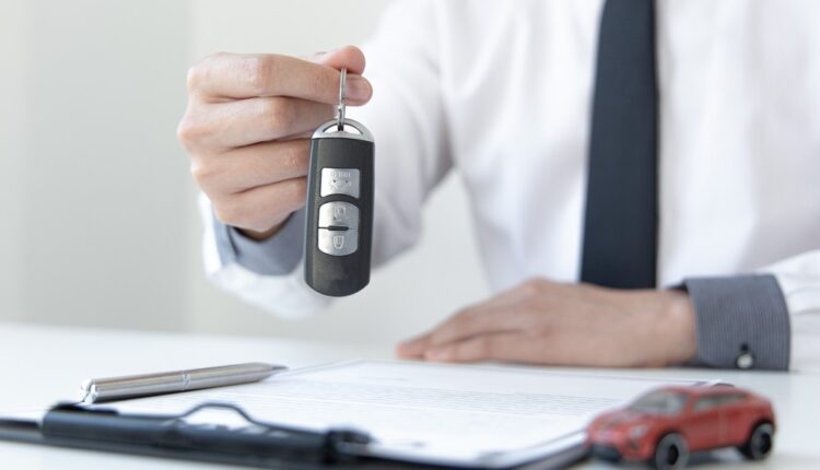 A person holding keys to a car, standing thoughtfully with paperwork and a car brochure, symbolizing the decision between car loan and leasing in the UAE.