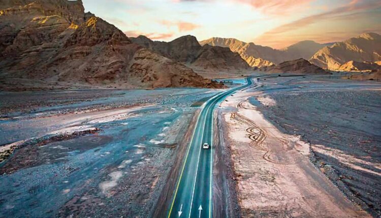 A silver luxury 4x4 SUV parked on a scenic overlook of the winding Jebel Jais mountain road during a golden winter sunset.