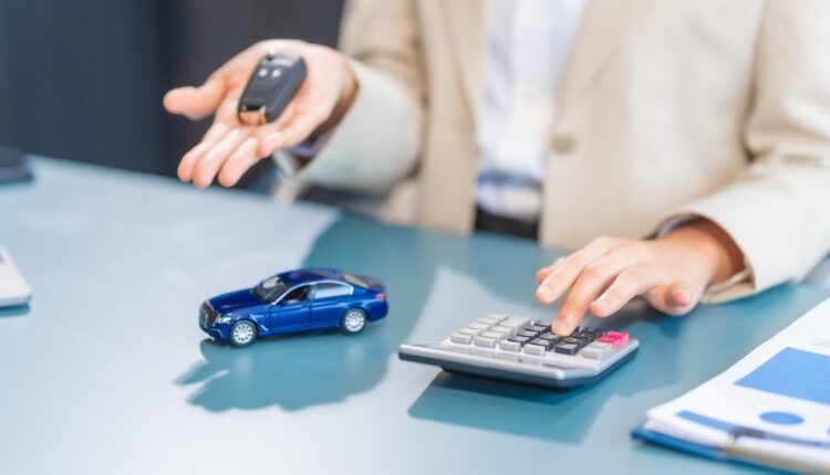 Person calculating car insurance cost in UAE with miniature car and key on desk