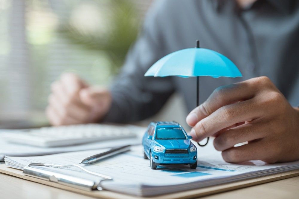 Toy car under a white umbrella symbolizing protection and comprehensive car insurance coverage in the UAE.