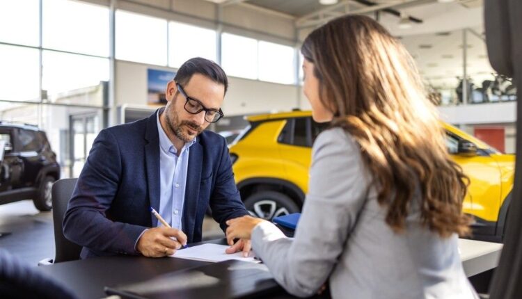 Car buyer signing auto loan financing agreement with sales advisor inside UAE car showroom