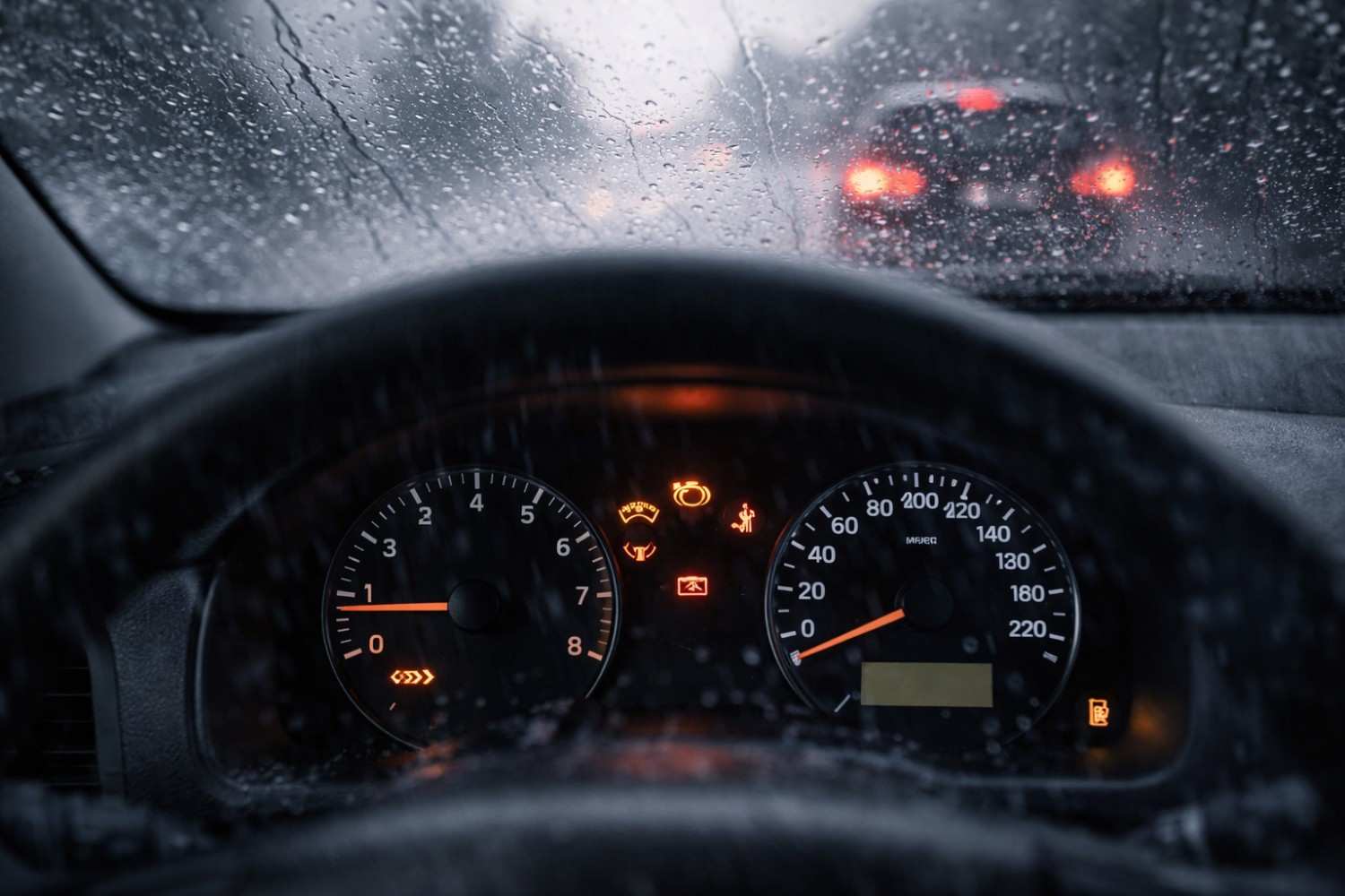 Close-up of a stalled car dashboard with warning lights illuminated during rainy conditions, showing the risks drivers face when a vehicle stops in floodwater| Arabwheels.ae