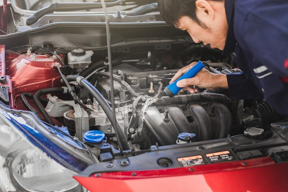 Mechanic inspecting used car engine with flashlight before purchase in the UAE| Arabwheels.ae