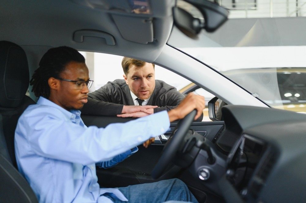 Car buyer testing the steering wheel while a salesperson explains vehicle features inside a Dubai showroom.| Arabwheels.ae