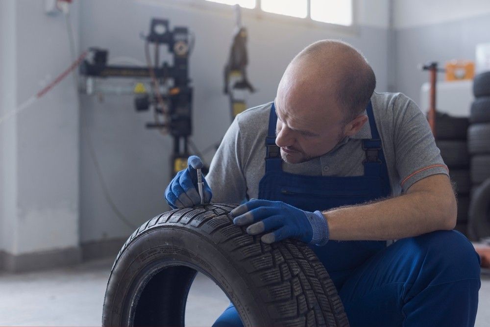 Mechanic inspecting tire tread depth to help UAE buyers check used car safety before purchase.| Arabwheels.ae