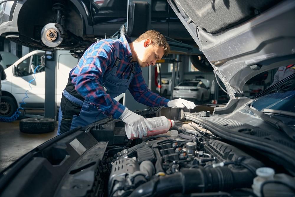 Mechanic checking a car cooling system in a garage to inspect radiator, coolant level, and overheating risk.|Arabwheels.ae