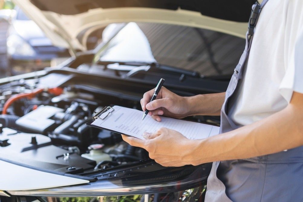 Mechanic inspecting a car engine with a checklist before UAE summer driving.|Arabwheels.ae