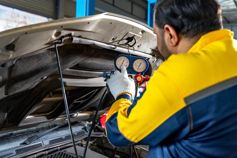 Technician checking car AC refrigerant pressure with manifold gauges in a workshop.|Arabwheels.ae