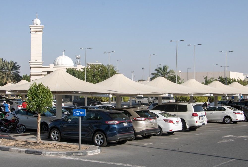 سيارات متوقفة تحت مظلات قرب مطار الشارقة مع ظهور لوحة مخرج|عرب ويلز
