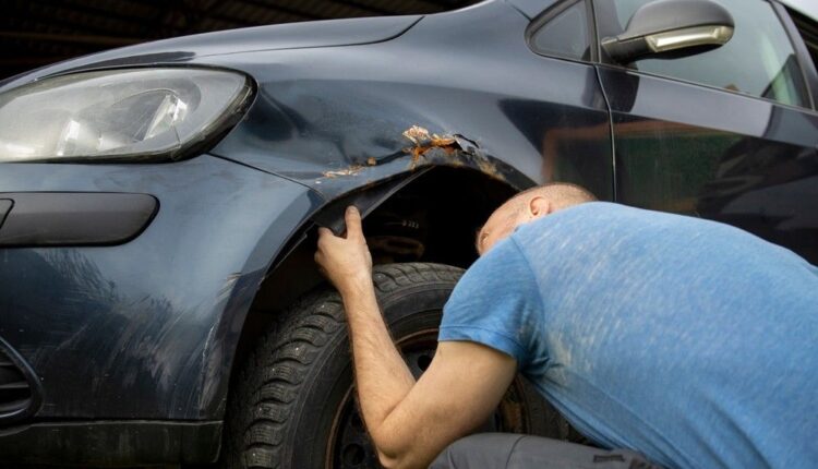 Mechanic inspecting a damaged front car fender near the wheel arch|Arabwheels.ae