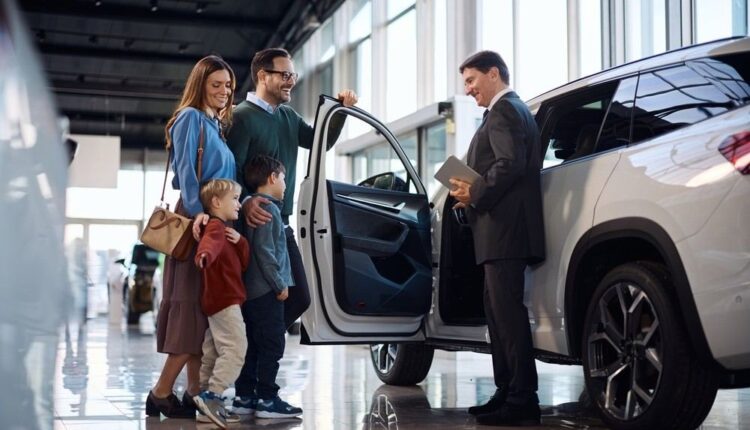 Family speaking with a car salesperson beside a new SUV in a showroom, illustrating the UAE new-car price war and current buying incentives.|Arabwheels.ae